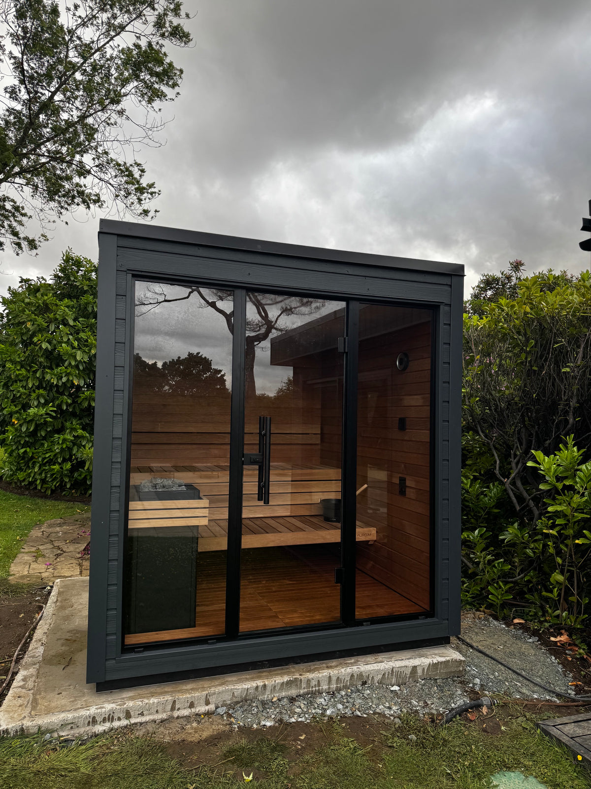 Completed residential garden sauna with dark cladding and a glazed front