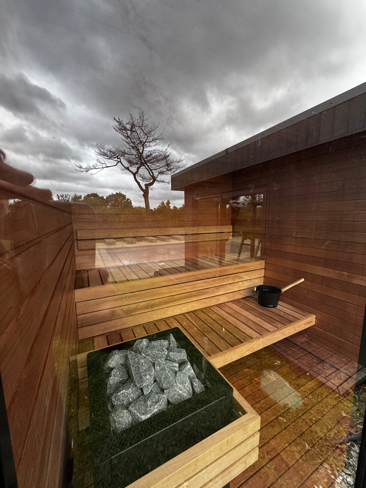 Timber benches, flooring and stone-filled sauna heater viewed through the glass